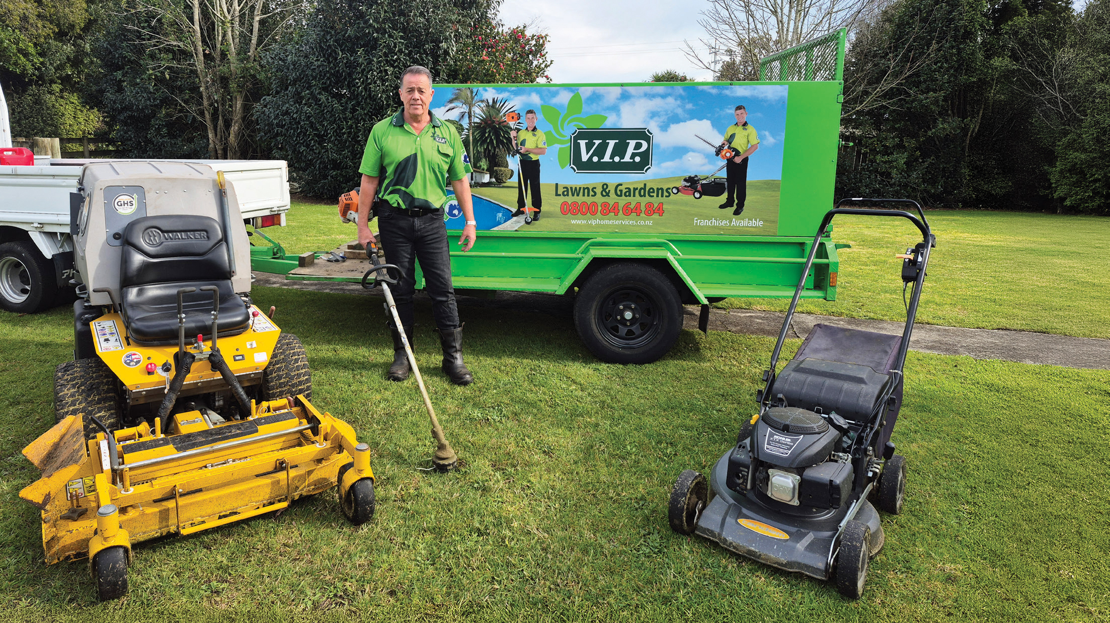 A V.I.P. Lawns & Gardens franchisee stands in front of his custom-built trailer with his ride-on and push mowers and weedeater 